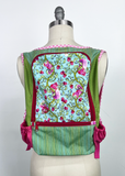 A handmade fabric carrier or pouch displayed on a cream dress form mannequin. The product features a light blue floral patterned front pocket with pink and green details, flanked by olive green mesh side panels and pink striped fabric trim.