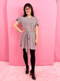 Woman in a gray dress standing in front of pink arches and pink carpet.